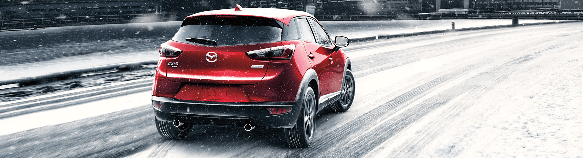 Mazda CX-3 rouge, vu de dos, un peu de biais, sur une route enneigée