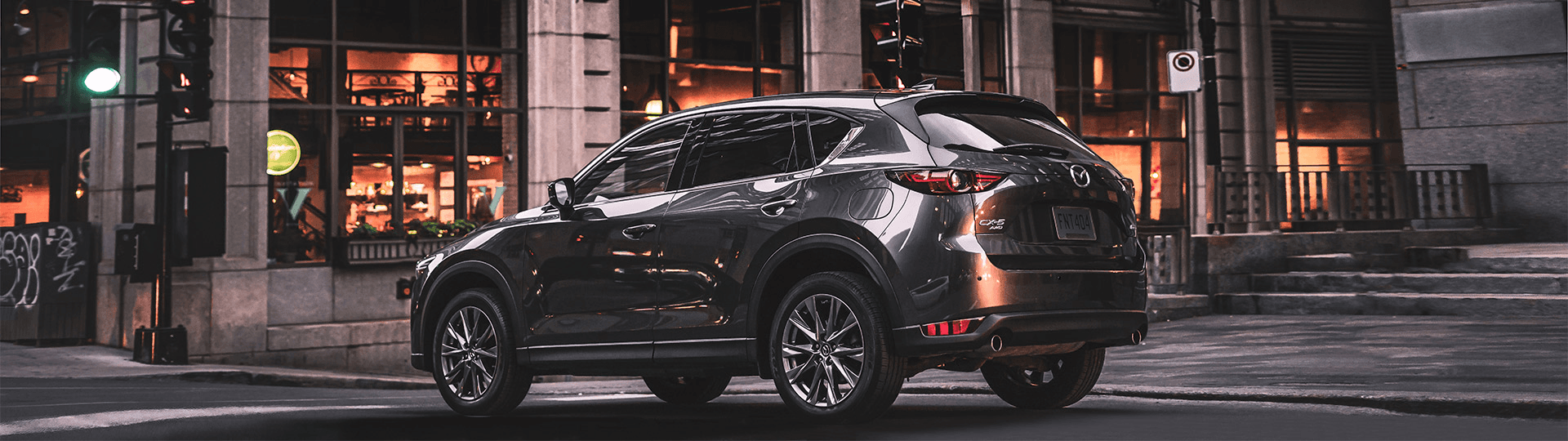 Mazda CX-5 2020 acier, vu de côté, un peu de dos, en ville à la brunante